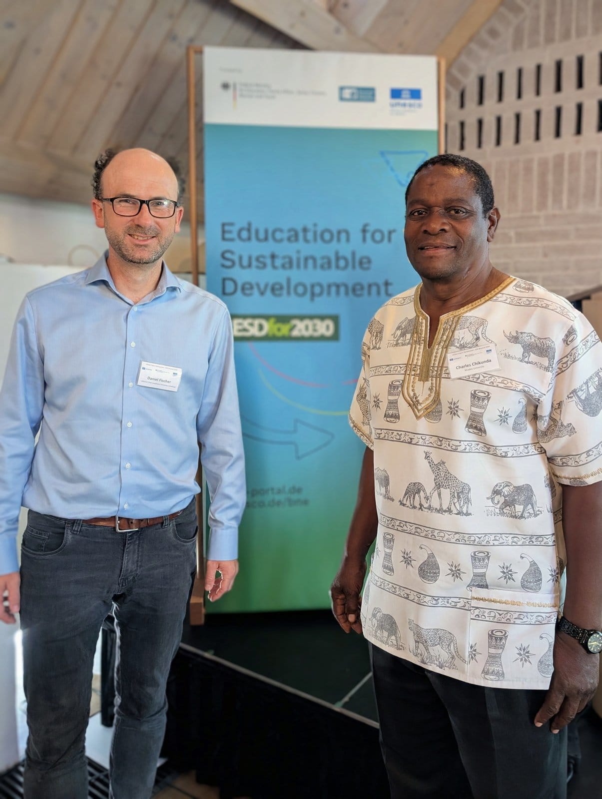 Daniel Fischer und Dr. Charles Chikunda vor dem ESD-for-2030-Banner beim Symposium in München